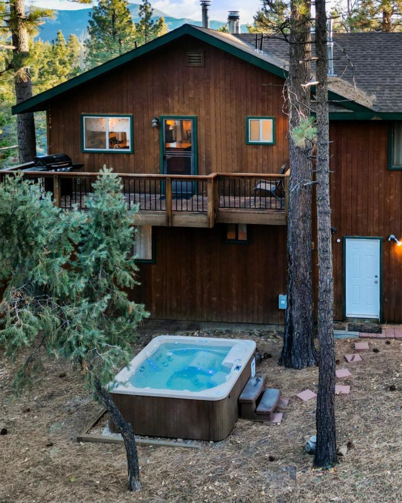 Bear Escapes cabin exterior featuring a private hot tub surrounded by tall pine trees in Big Bear Lake.