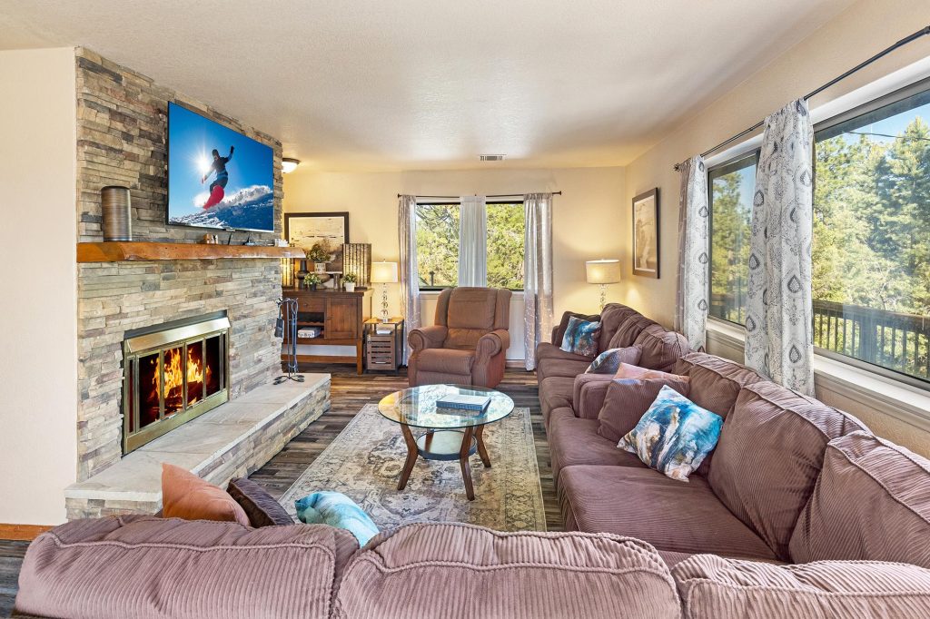 Cozy Bear Escapes living room with a stone fireplace, comfortable seating, and forest views.