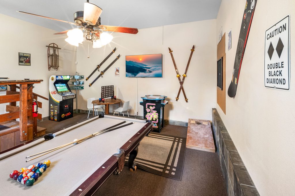 Game room at a Bear Escapes cabin featuring a pool table, arcade games, and mountain-themed décor.