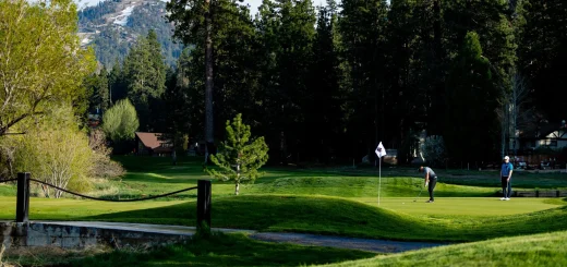 Two golfers play on a green course at Big Bear with forested mountains in the background.