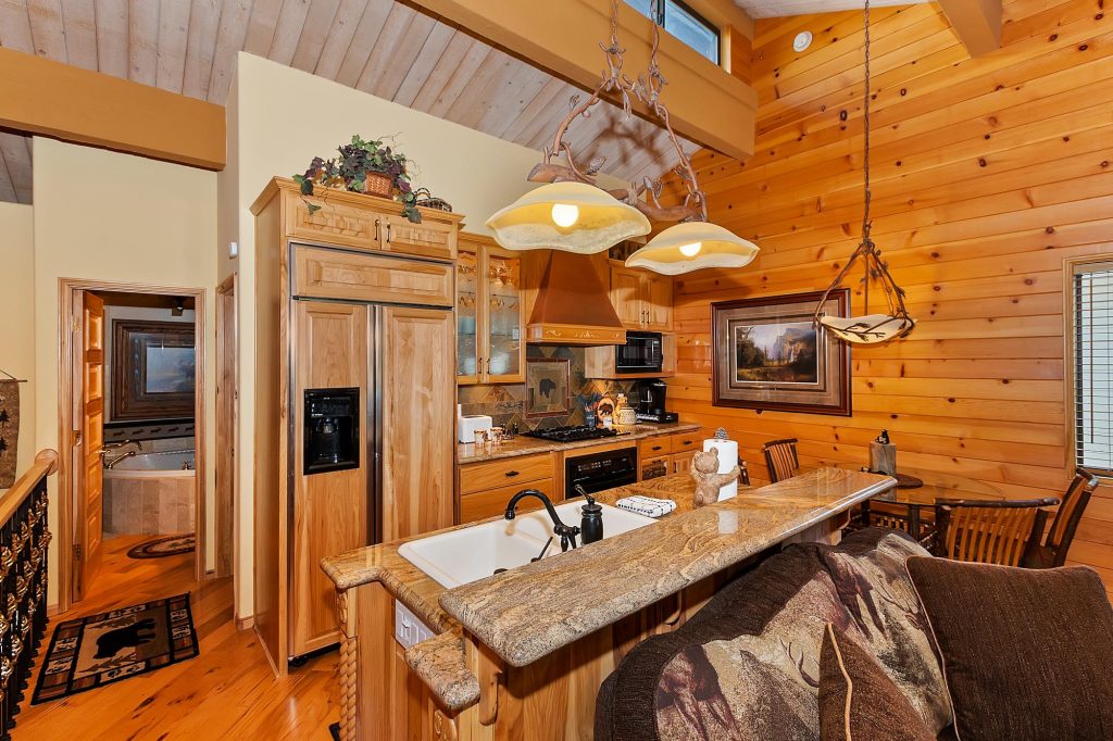 Modern rustic cabin kitchen with wood interiors, granite countertop, open concept dining area, and warm lighting mountain retreat home