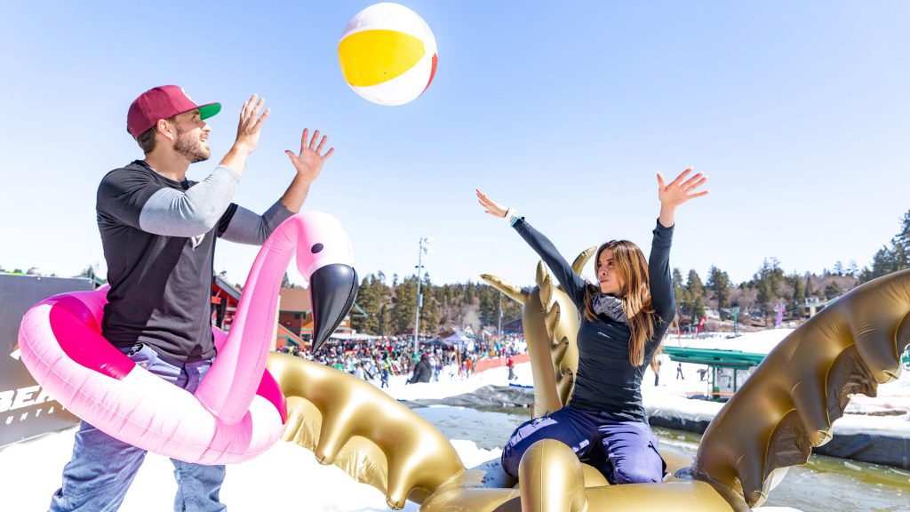 A man and woman with inflatable toys play with a beach ball in the snow at the Bear Break event in Big Bear.