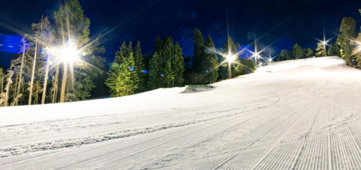 Floodlit ski slope at night at Big Bear Mountain Resort with groomed snow and pine trees in the background.