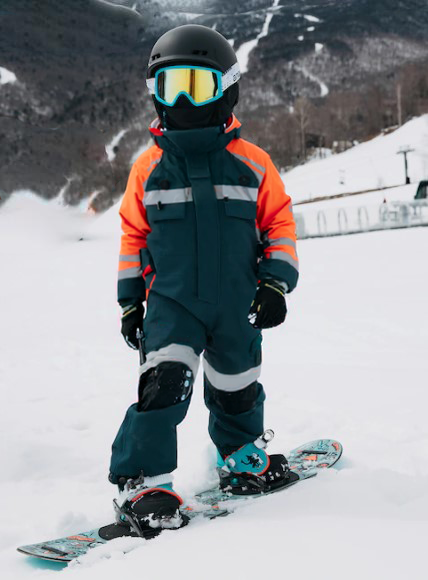 Child on a snowboard on the side of ski slope wearing snow gear.