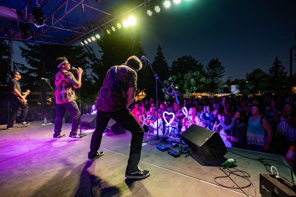 Live band performing on stage in front of a crowd during an outdoor nighttime concert in Big Bear Lake