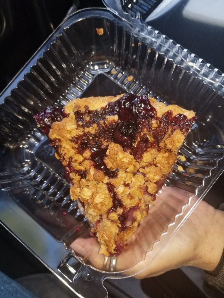 Hand holding a berry crumb bar with visible oat crumble and jam filling in a plastic container.
