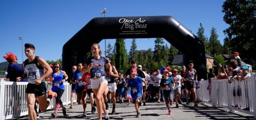Group of runners starting a road race under a large inflatable “Open Air Big Bear” arch, with participants wearing race bibs and running through a fenced start corridor on a sunny day.