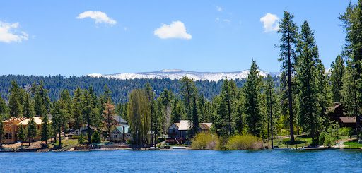 Green scenery in front of the Big Bear Lake and several houses next to tall trees.