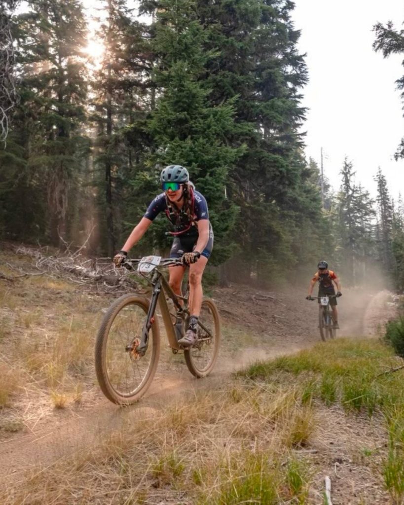 Two mountain bikers race along a dusty forest trail surrounded by tall pine trees in Big Bear.
