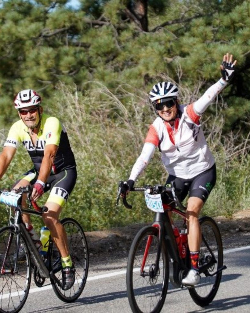 Two cyclists ride along a scenic road in Big Bear, smiling and enjoying a recreational cycling event.