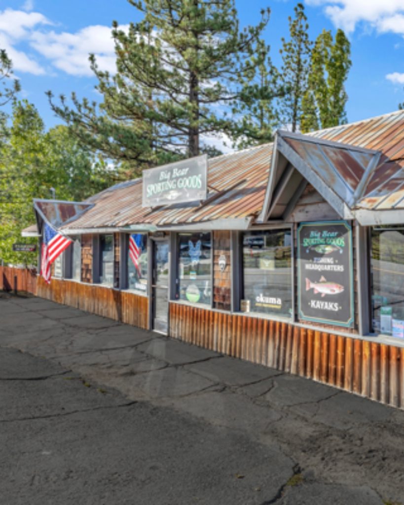 Exterior view of Big Bear Sporting Goods store with rustic mountain-style architecture, American flags, and outdoor sporting equipment signage.