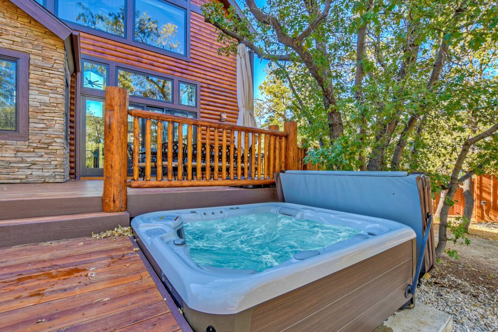 A hot tub with bubbling water is shown on a wooden deck next to a rustic cabin with log railings, located at Big Bear.