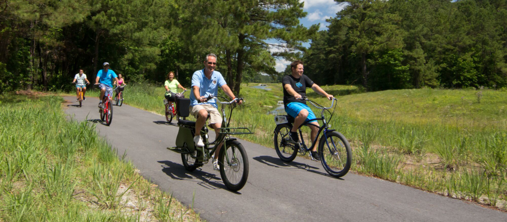 A group of people enjoy a leisurely bike ride on a paved path through a grassy, wooded area at Big Bear.