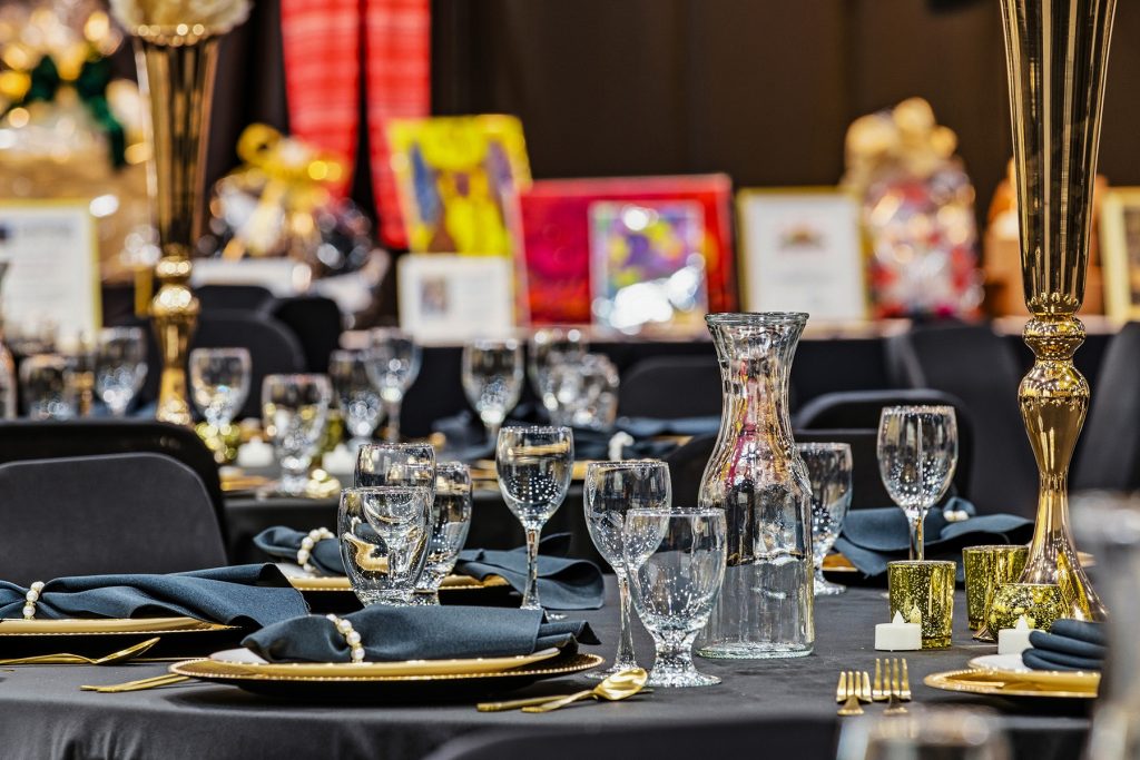 Elegant banquet table setup with black linens, gold accents, and glassware centerpiece