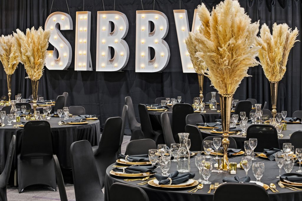 Banquet tables with illuminated backdrop and elegant centerpiece arrangements
