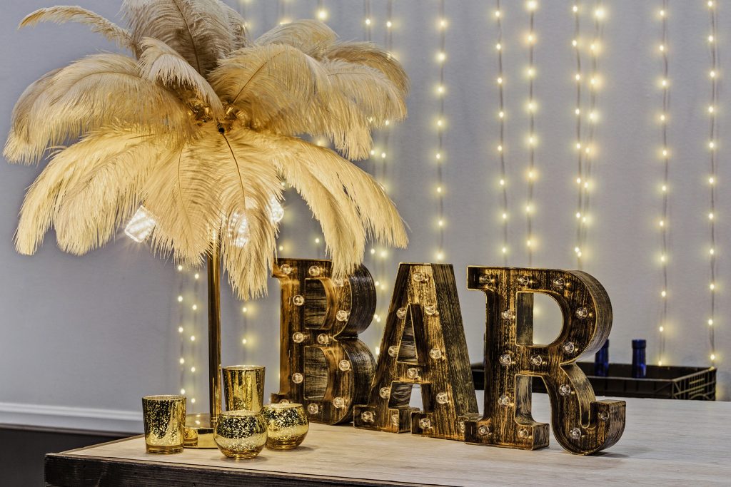 Decorative BAR sign with warm lights, gold candle holders, and feather centerpiece