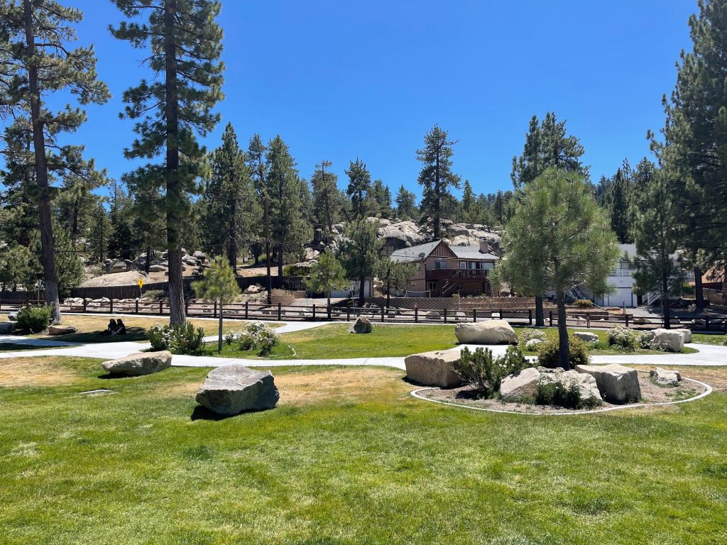 Landscaped grounds at Boulder Bay Park featuring green lawns, walking paths, pine trees, decorative boulders, and mountain scenery in Big Bear.