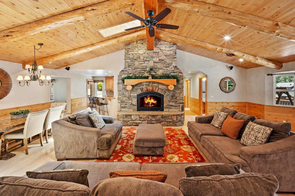 Spacious luxury cabin living room with stone fireplace, wooden ceiling, rustic furniture, and cozy mountain lodge interior design