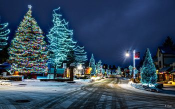 Snowy Big Bear village street glowing with colorful Christmas lights and decorated trees at night.
