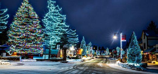 Snowy Big Bear village street glowing with colorful Christmas lights and decorated trees at night.