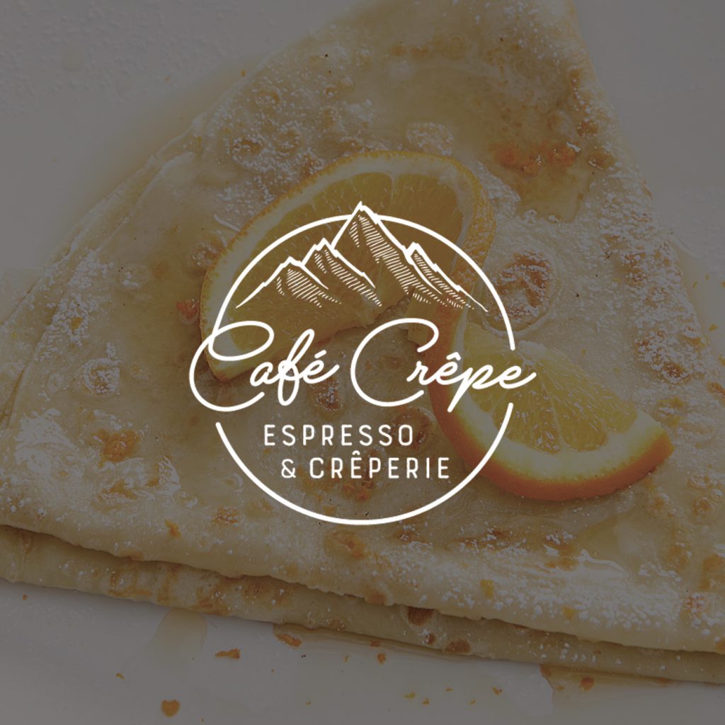 A crepe garnished with an orange slice and powdered sugar is shown on a white plate from Café Crêpe Espresso & Crêperie at Big Bear.