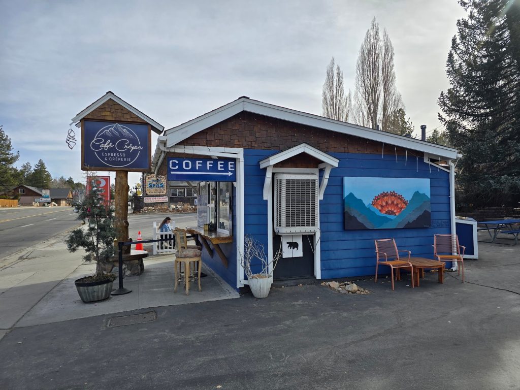 Front view of Café Crêpe building with blue siding, signage, and outdoor seating.