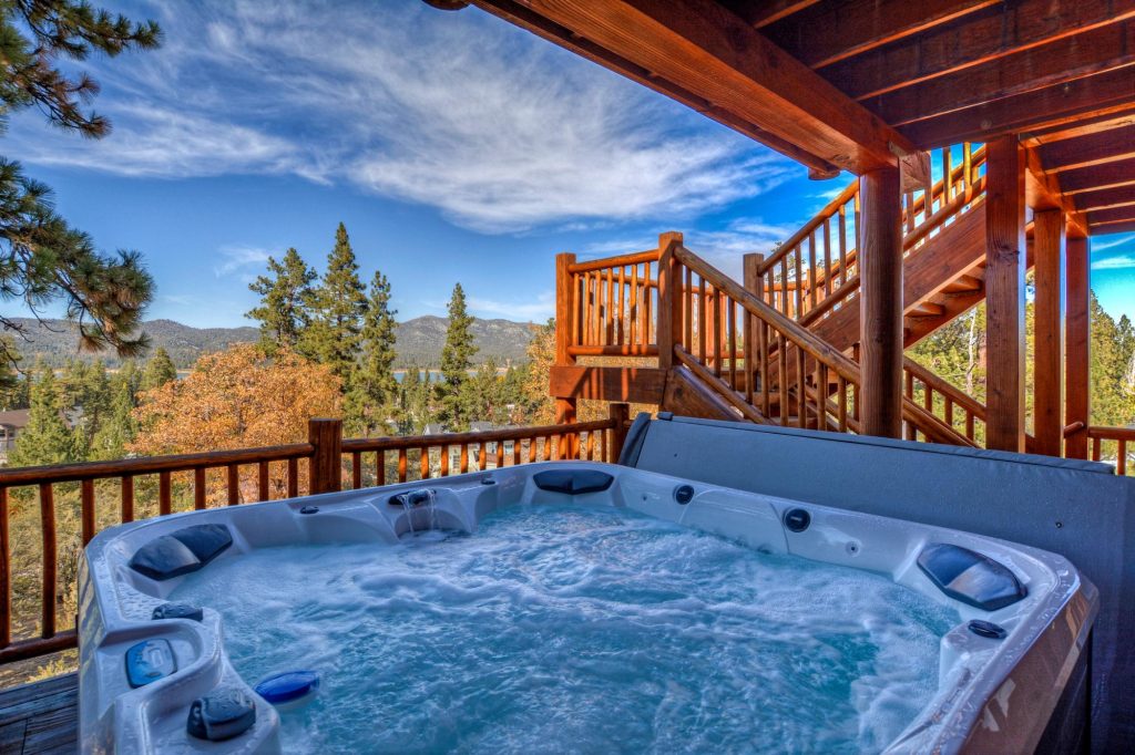 Outdoor hot tub on a covered deck with mountain and lake views surrounded by pine trees