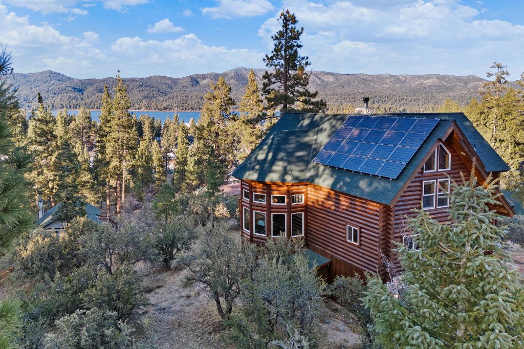 Log cabin surrounded by pine trees with lake and mountain views in the distance