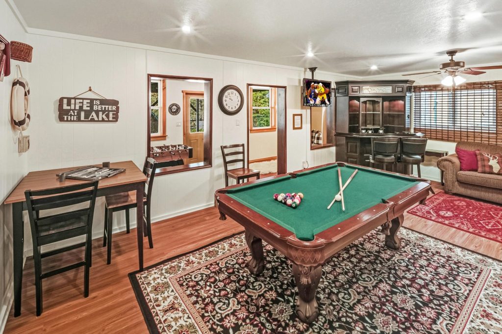 Cozy cabin game room featuring a pool table, seating area, bar counter, and entertainment setup with rustic interior decor