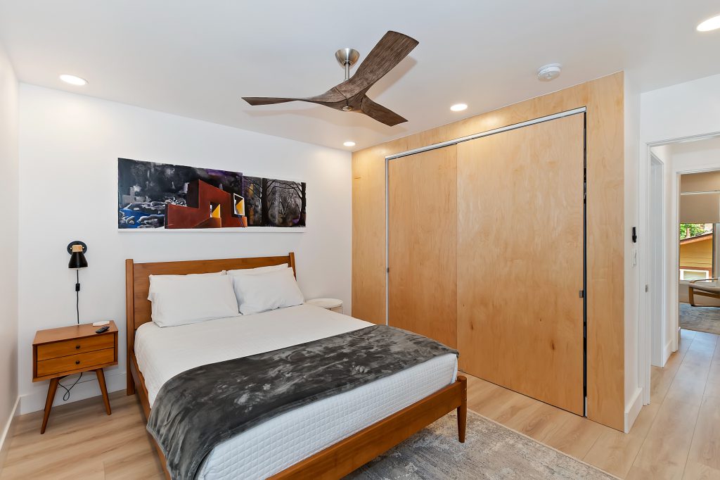 A cozy bedroom with a modern wooden bed, a ceiling fan, and light wood closet doors in Big Bear.