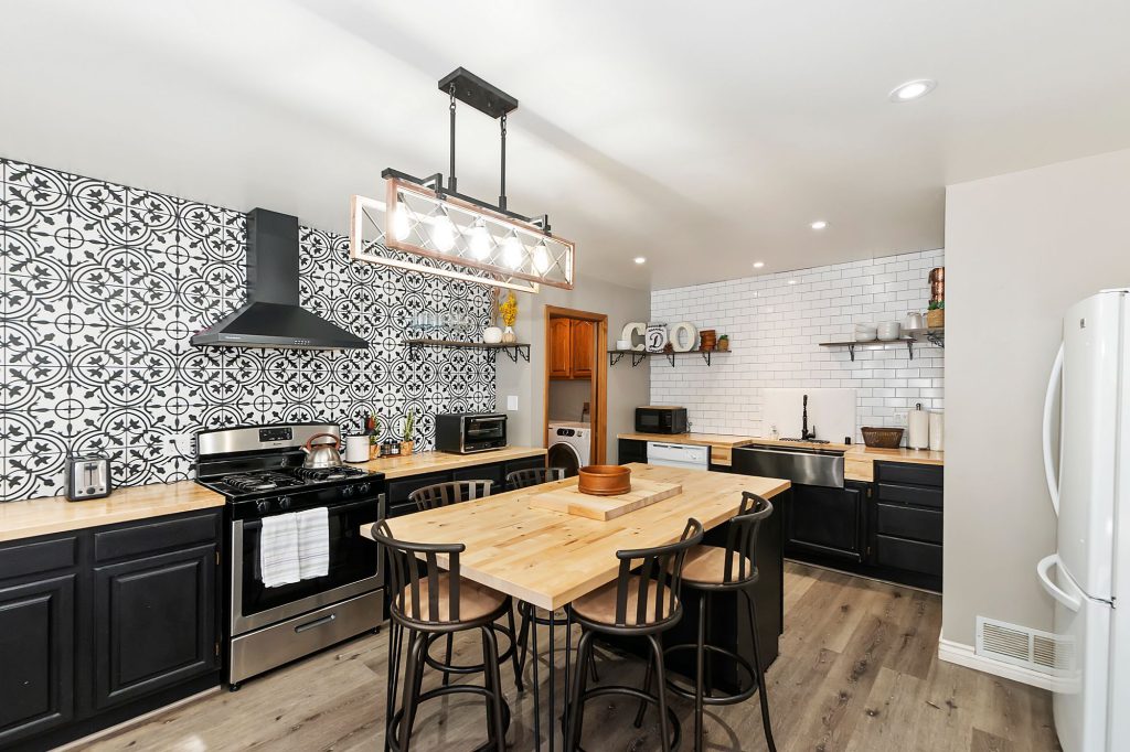 Kitchen with black and white tiles behind the a butcher block counter and black cabinets. A center island with black chairs