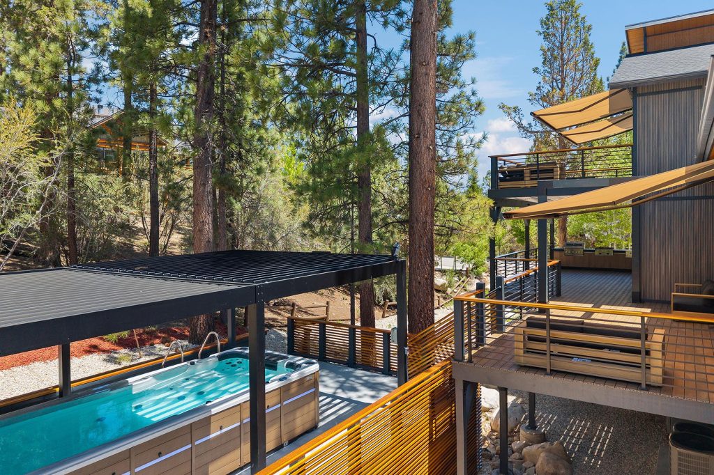Covered outdoor jacuzzi area with modern deck and pine trees at a Big Bear mountain cabin