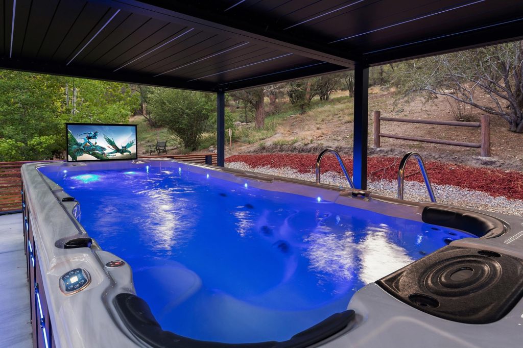 Covered swim spa at Castlewood Pines glowing at night with LED lighting and forest surroundings.