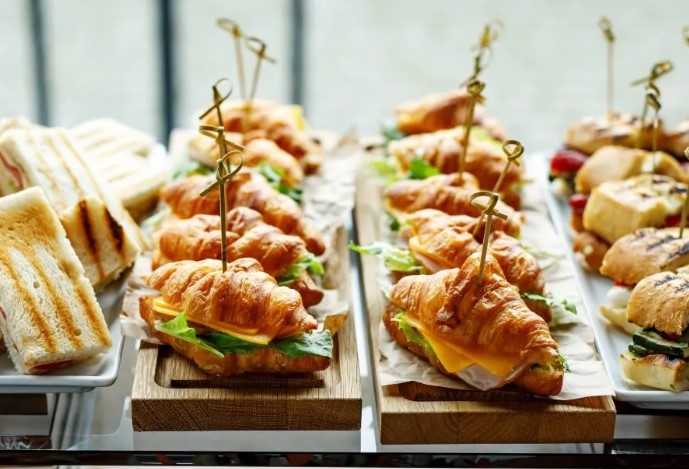 An image of a variety of croissant sandwiches and other small sandwiches, arranged on platters.