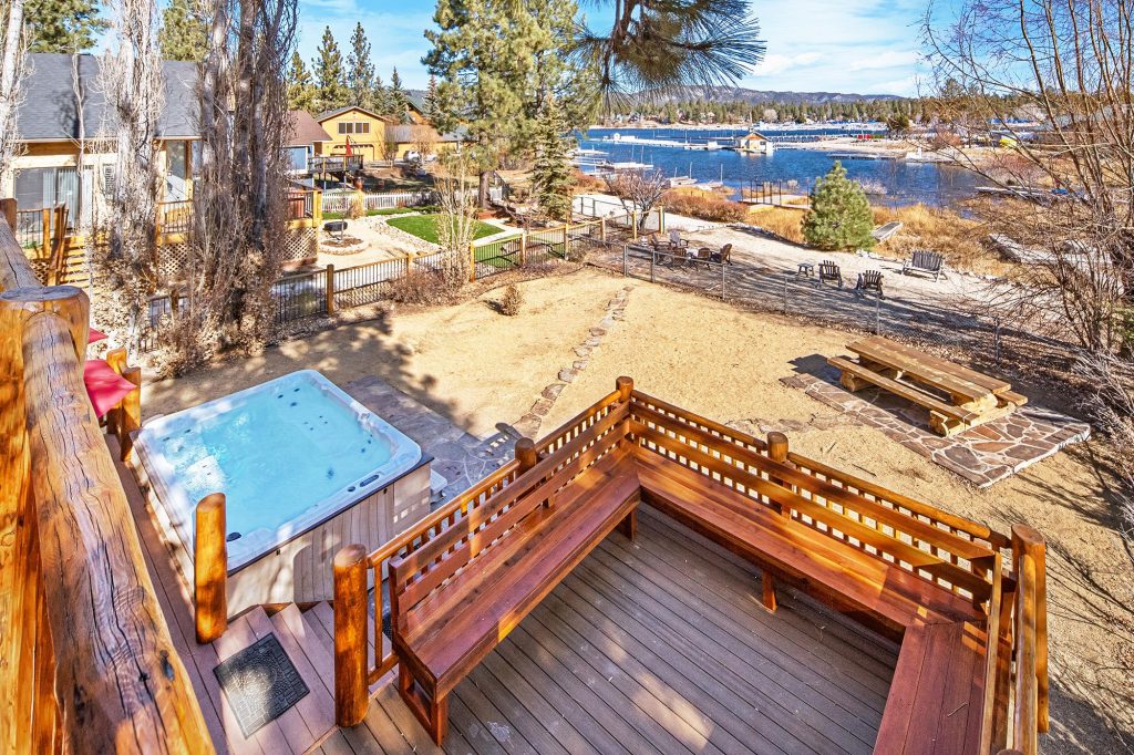 Scenic backyard view with a wooden deck, hot tub, fenced yard, and lake in the background