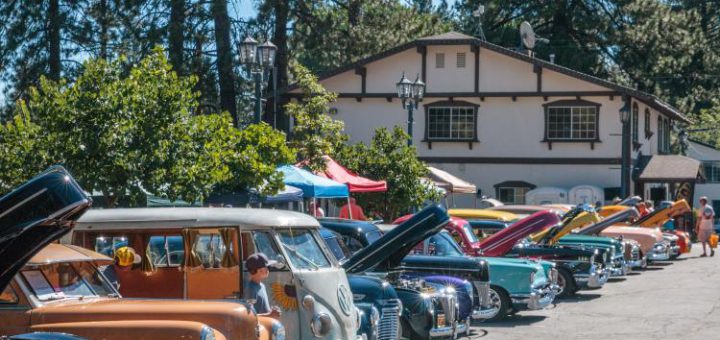 A line of classic cars, including a VW bus and a vintage woody wagon, are on display at a car show in Big Bear.