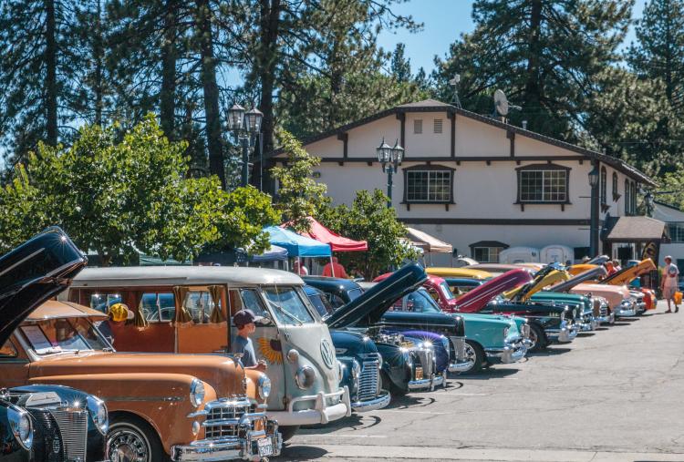 A line of classic cars, including a VW bus and a vintage woody wagon, are on display at a car show in Big Bear.