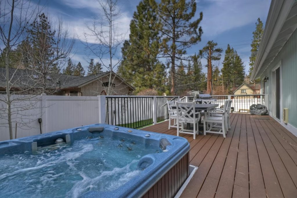 Big Bear cottage with a spacious outdoor deck, bubbling hot tub, dining table, and pine tree surroundings