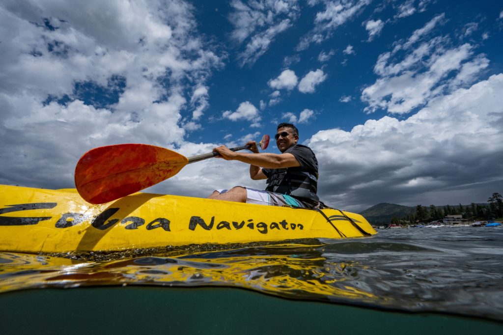 Man kayaking on a lake in a yellow kayak under dramatic cloudy sky with scenic mountain and water views