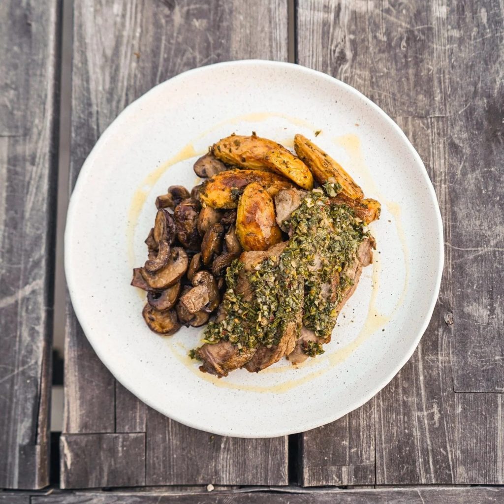 Herb-crusted meat served with roasted potatoes and sautéed mushrooms on a white plate
