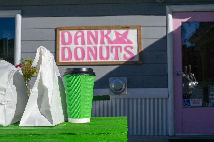 A green coffee cup and white paper bags are shown on a bench in front of the Danky Donuts shop in Big Bear.