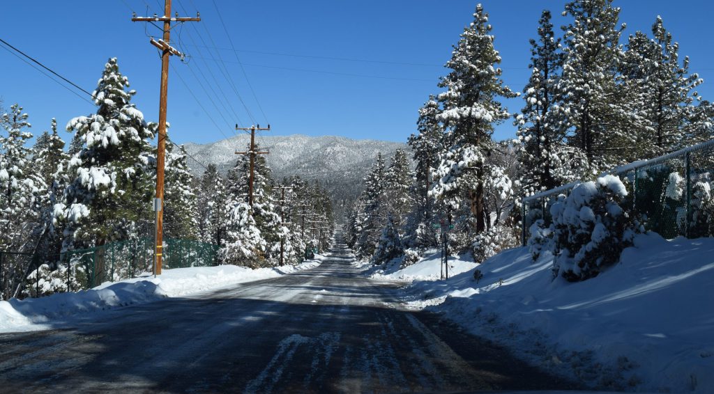 Snow-covered road alongside a power line, set in the scenic landscape of Big Bear Lake.