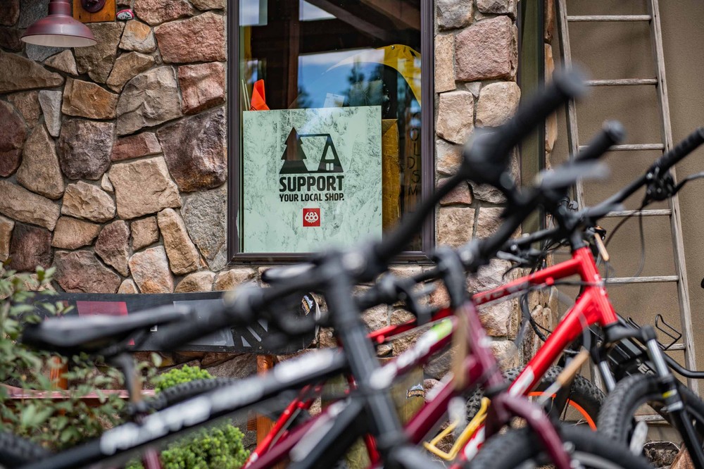 close-up shot of several bicycles parked outside a stone-walled building in Big Bear, with a sign in the window that reads, "SUPPORT YOUR LOCAL SHOP.