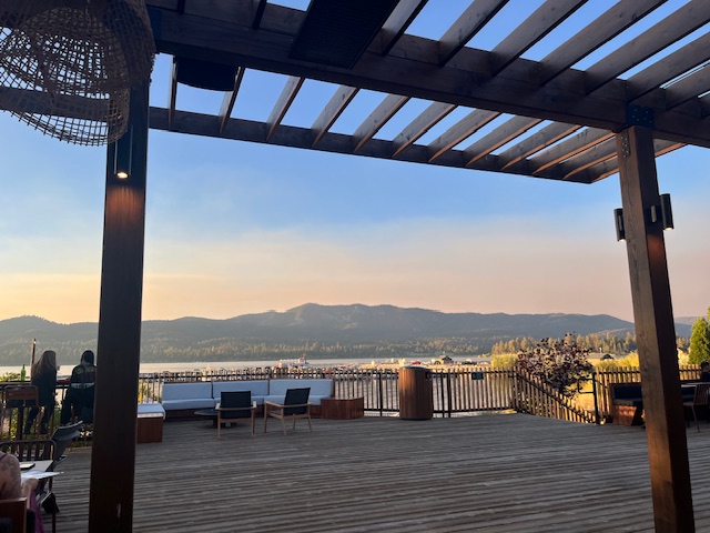 An outdoor deck at Big Bear with a wooden pergola and lounge furniture, offering a scenic view of the lake and mountains at sunset.