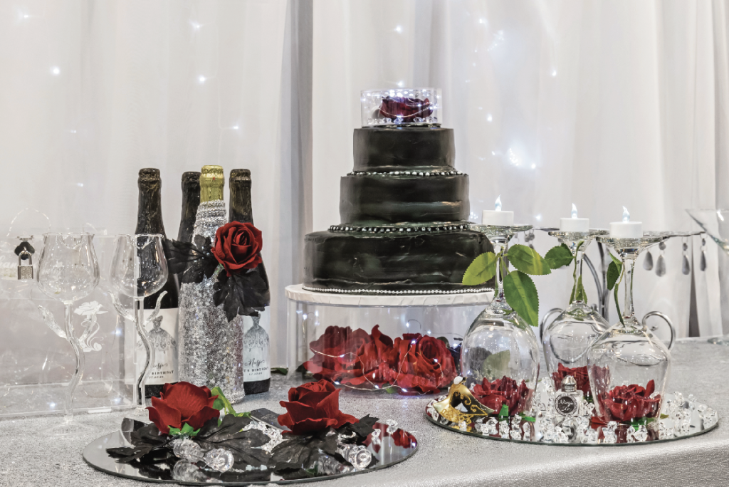 A beautiful black and silver tiered cake is the centerpiece of a decorated table, surrounded by wine bottles, red roses, and glasses for a wedding or special event in Big Bear.