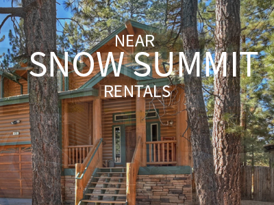 A large, wooden cabin with stone accents and a front deck is framed by two tall pine trees. The text "NEAR SNOW SUMMIT RENTALS" is overlaid on the image.
