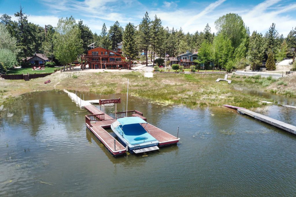 An aerial view of a lakefront cabin in Big Bear with a covered boat on a private dock extending out into a lake.