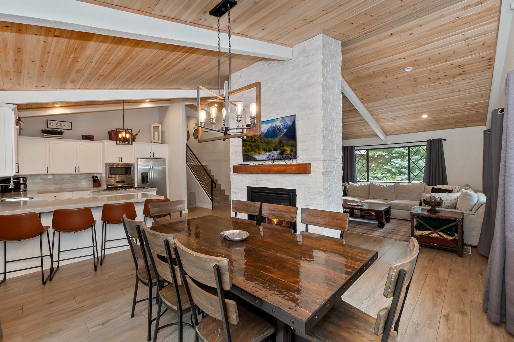 Modern open-concept dining room, kitchen, and living area with fireplace and vaulted wood ceiling