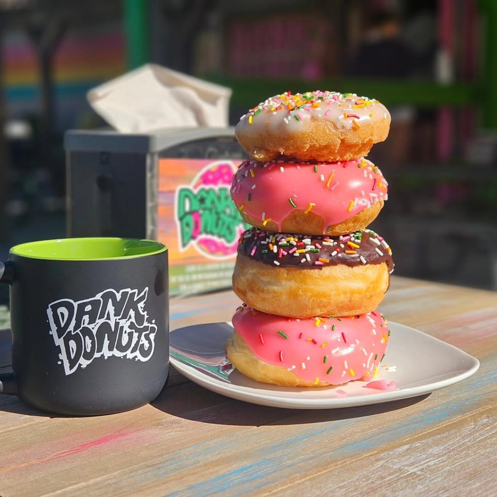 Stack of colorful sprinkled donuts on a plate beside a coffee mug on an outdoor table.