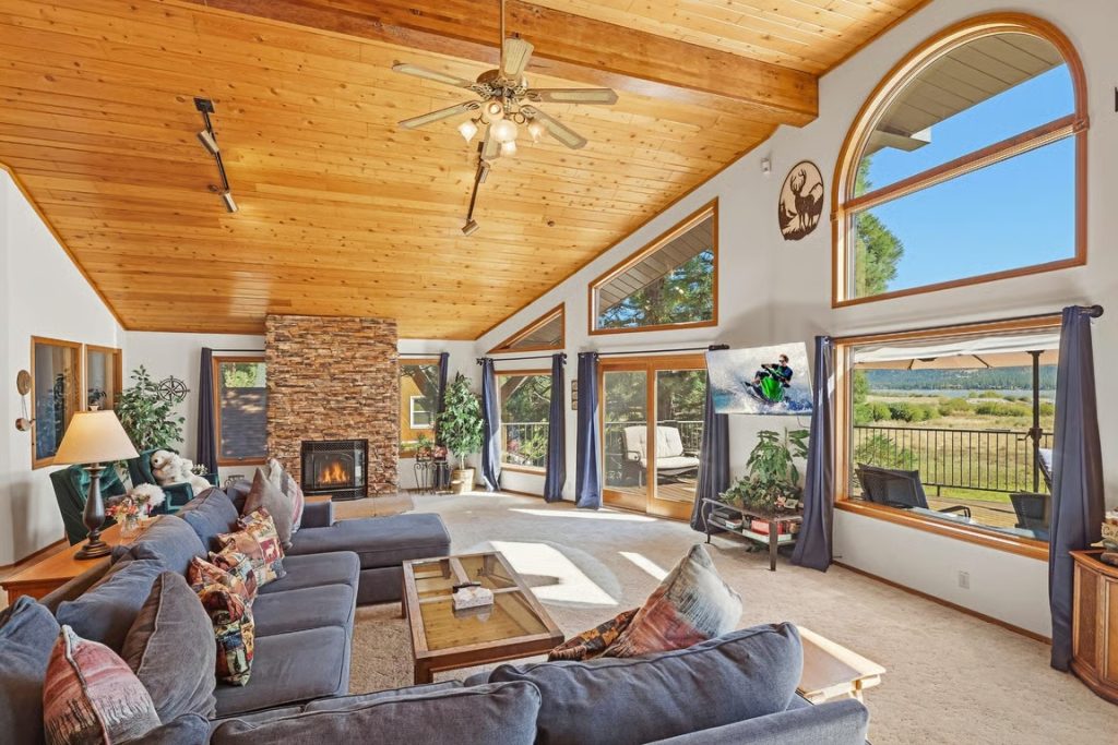 Spacious Eagle Manor cabin living room in Big Bear featuring vaulted wood ceilings, a stone fireplace, comfortable sofas, and large windows with scenic views.